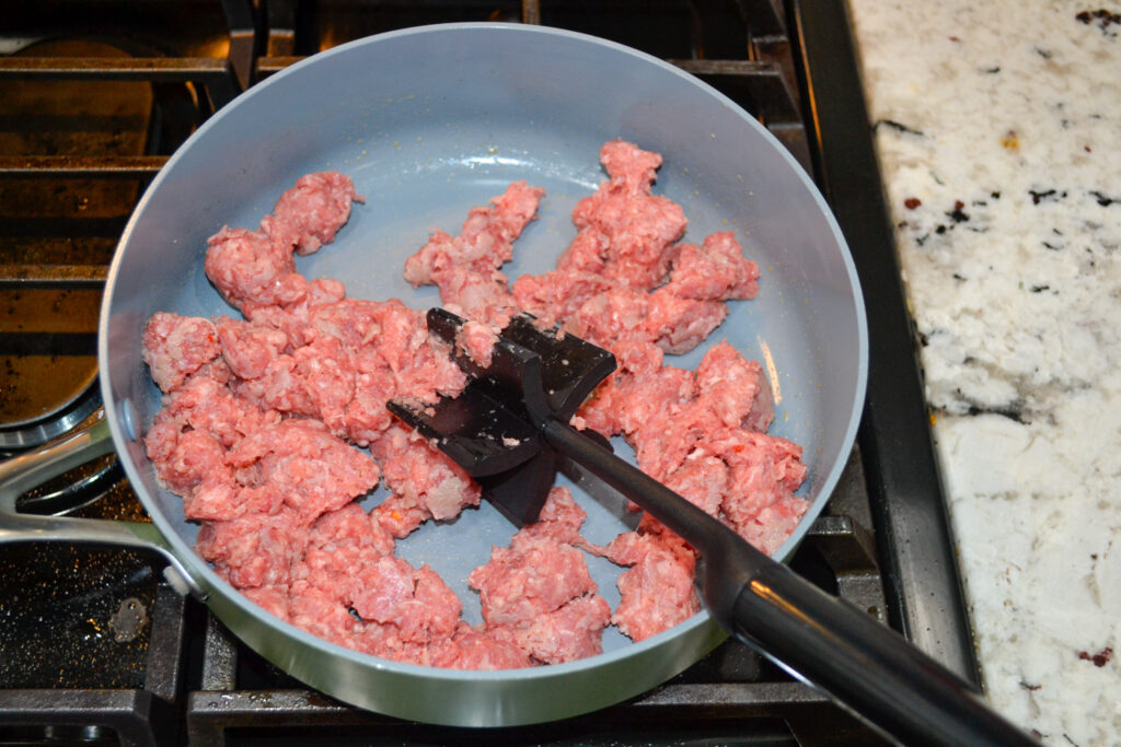 Breakfast sausage browning in a skillet with a meat chopper