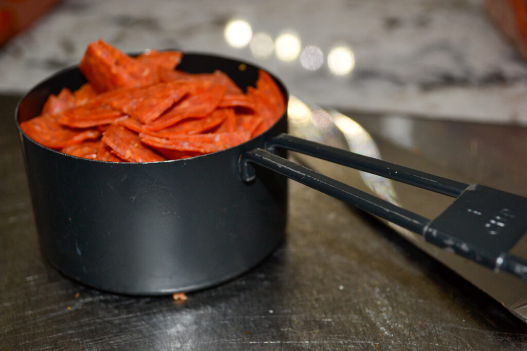 Measuring cup filled with pepperoni for pizza pinwheels