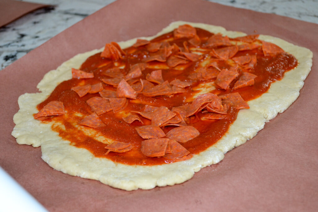 Pepperoni layered over pizza sauce on rolled-out dough