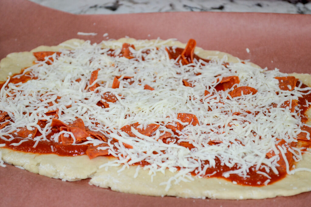 Shredded mozzarella sprinkled over pepperoni and pizza sauce on pizza dough
