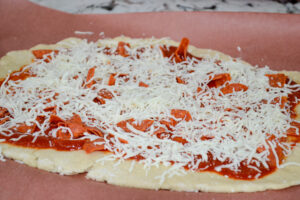 Shredded mozzarella sprinkled over pepperoni and pizza sauce on pizza dough