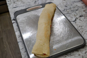 Pizza dough rolled up tightly into a log on a baking sheet
