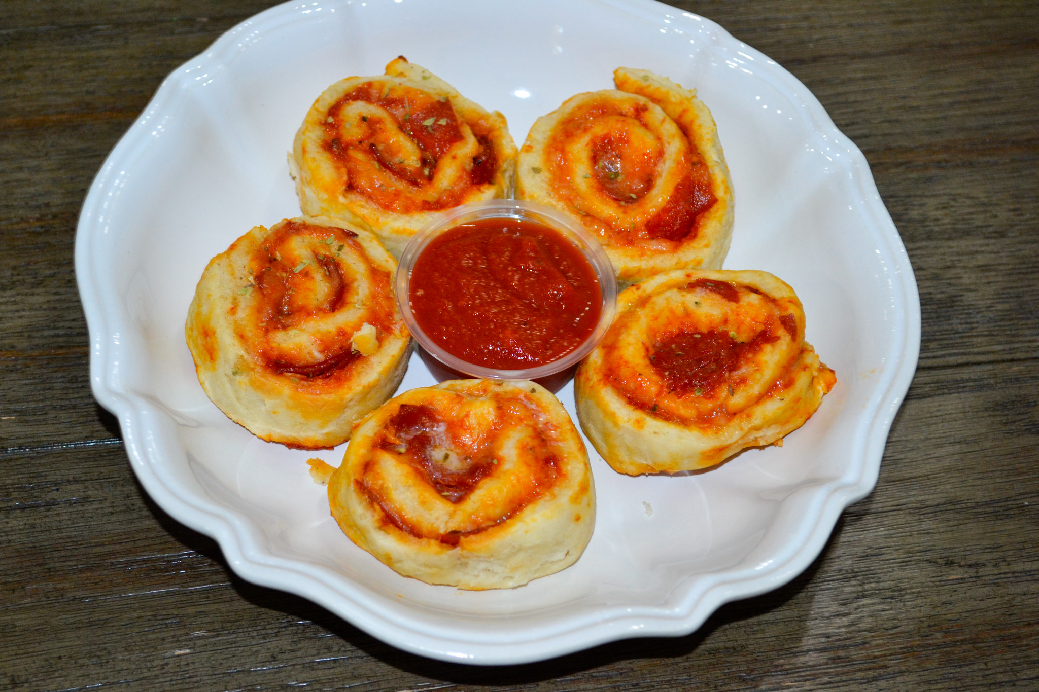 Pepperoni pizza pinwheels on a white plate with marinara for dipping