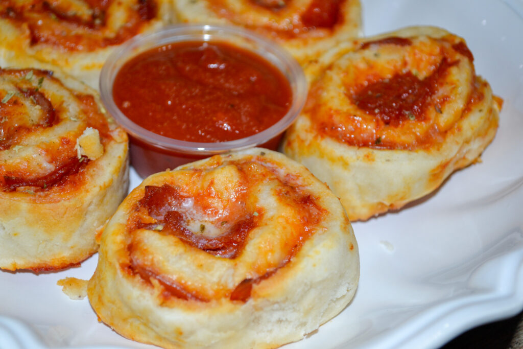 Close-up of pizza pinwheels on a plate with a cup of pizza sauce