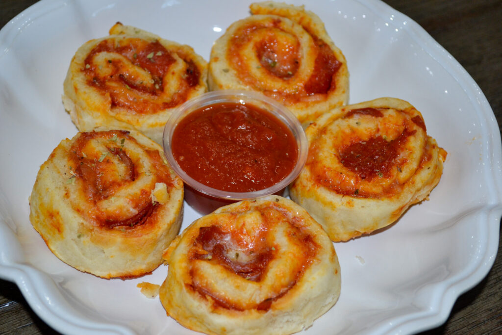 Plate of cheesy pepperoni pizza pinwheels around a cup of dipping sauce
