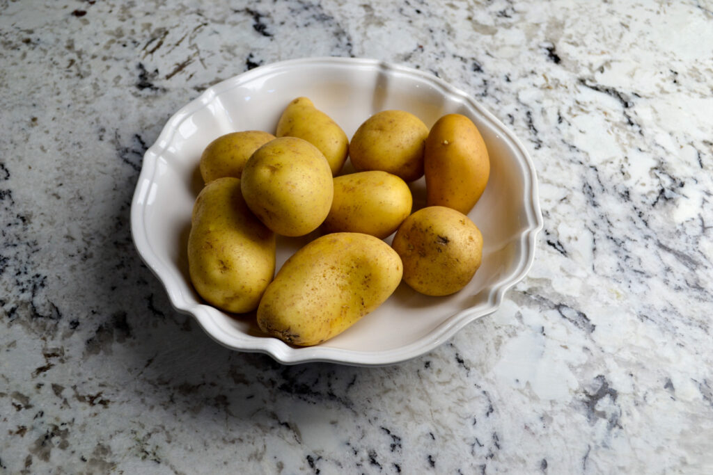 Whole potatoes in a white scalloped bowl on a granite countertop
