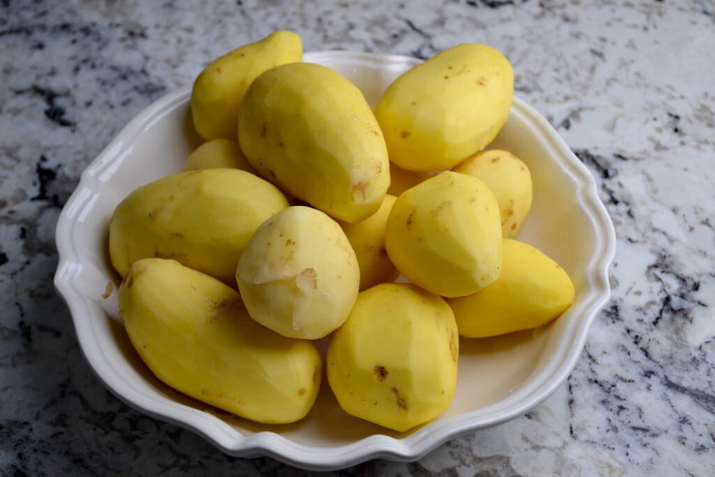 Peeled potatoes in a white bowl on a granite countertop