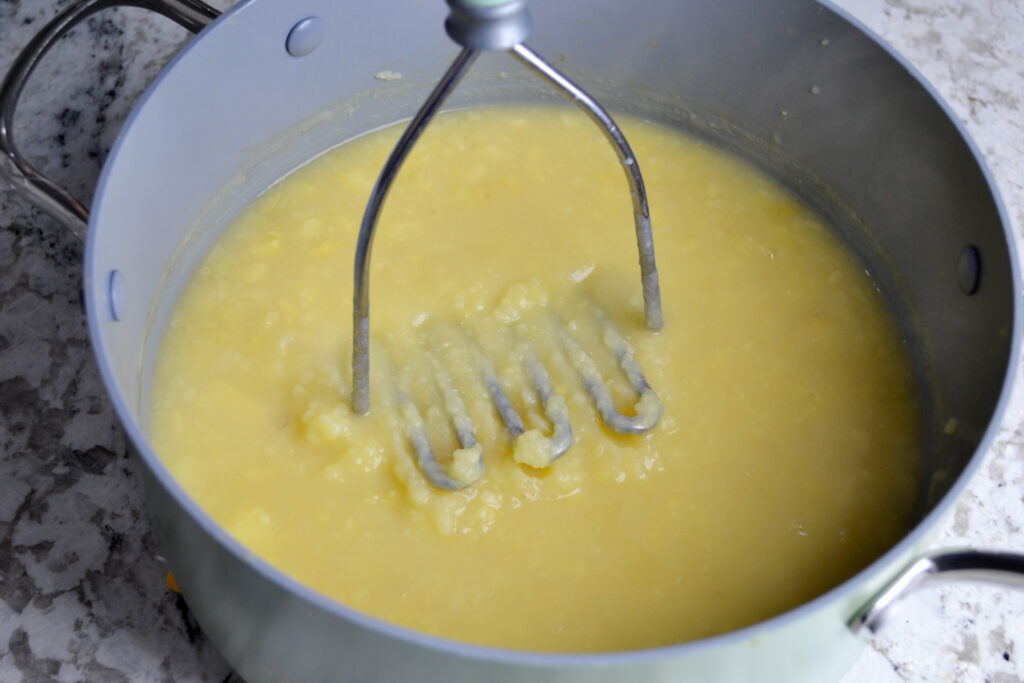 Potato masher mashing cooked potatoes in broth in a large pot