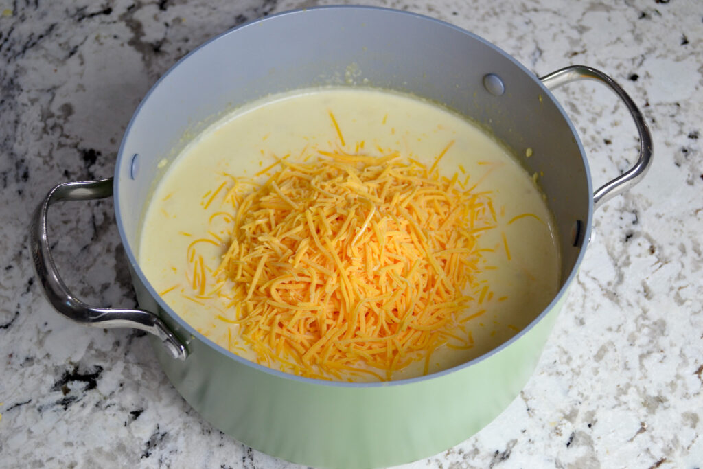 Shredded cheddar cheese added to creamy potato soup in a pot