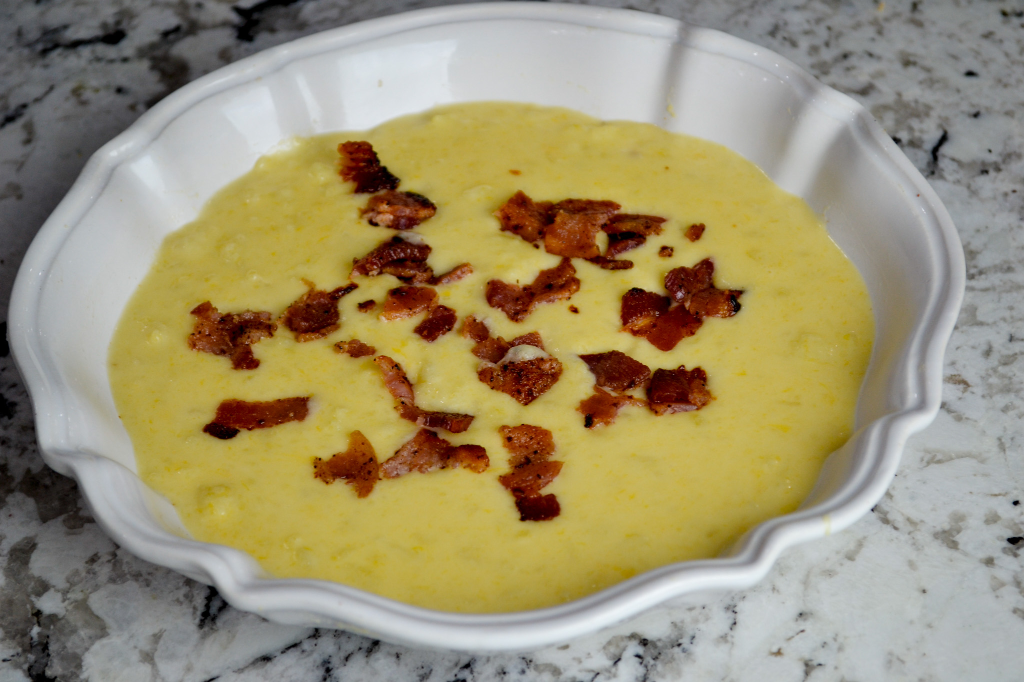 Bowl of the best potato soup topped with crispy bacon on a granite countertop