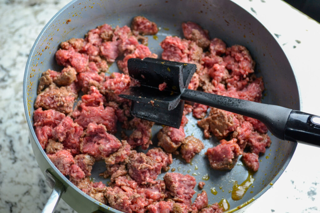 Raw ground beef browning in a large pot for taco soup