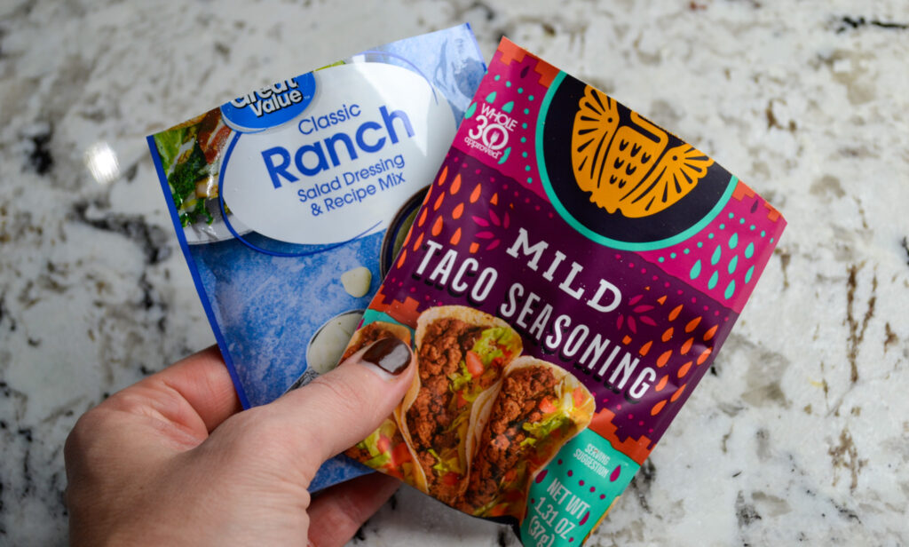 Hand holding a ranch seasoning packet and a mild taco seasoning packet