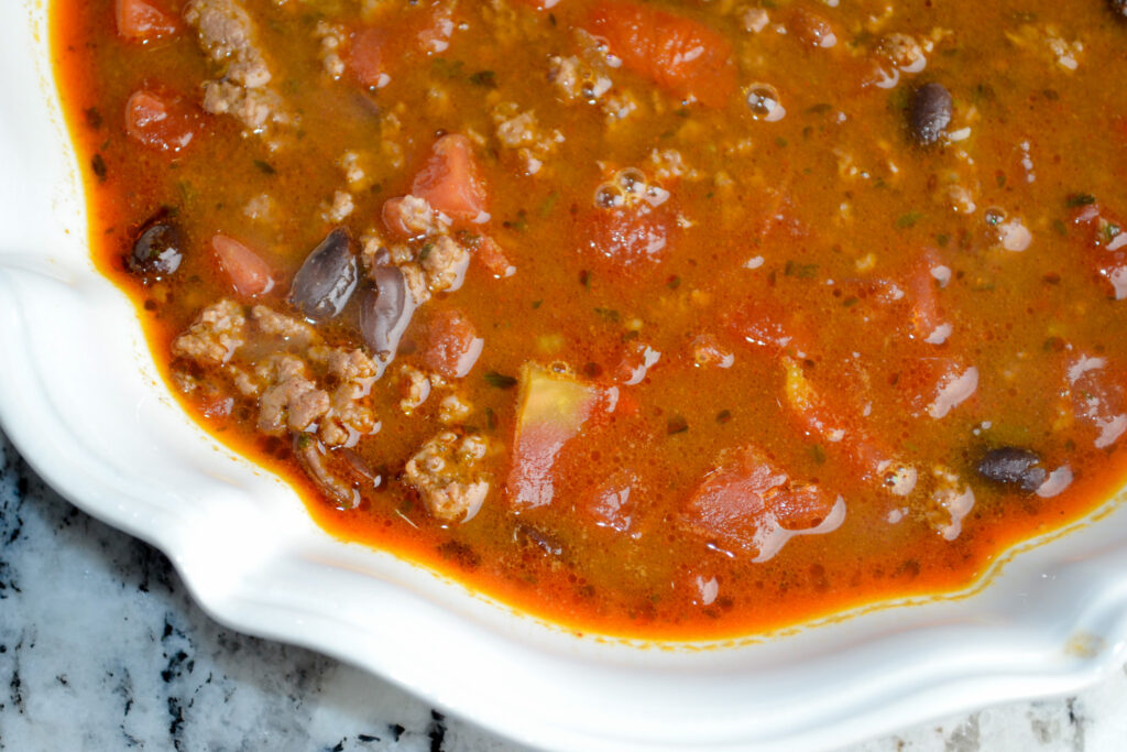 Taco soup with ground beef, black beans and tomatoes in a white bowl