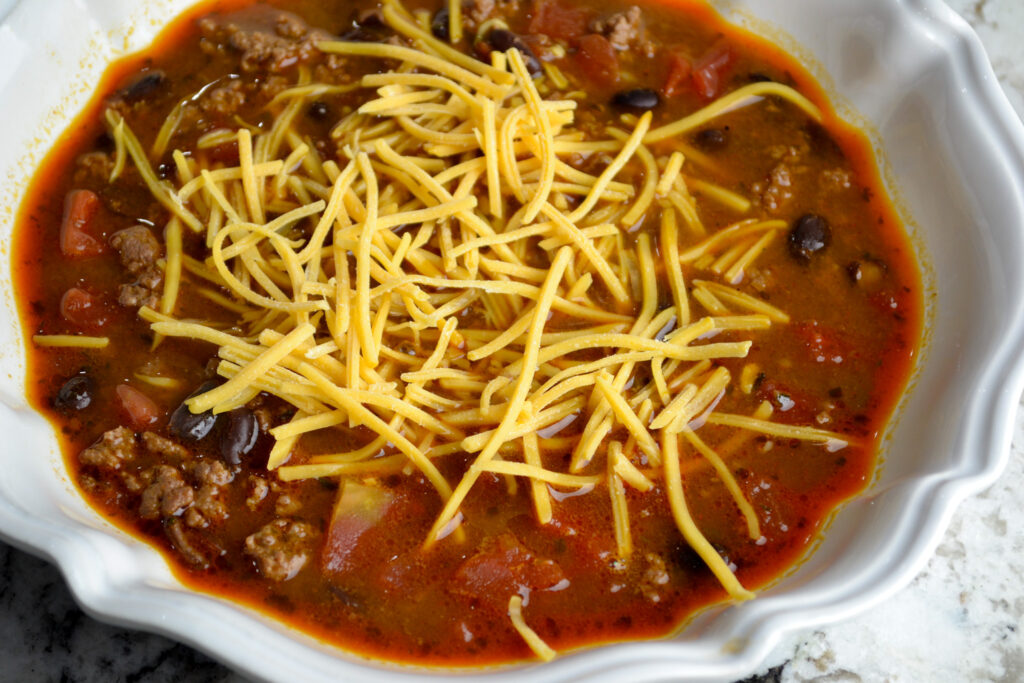 Easy taco soup topped with shredded cheddar cheese in a white bowl