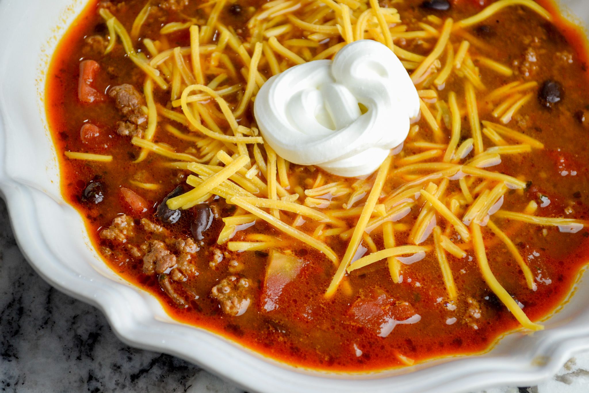 Easy taco soup with ranch topped with shredded cheddar and a dollop of sour cream
