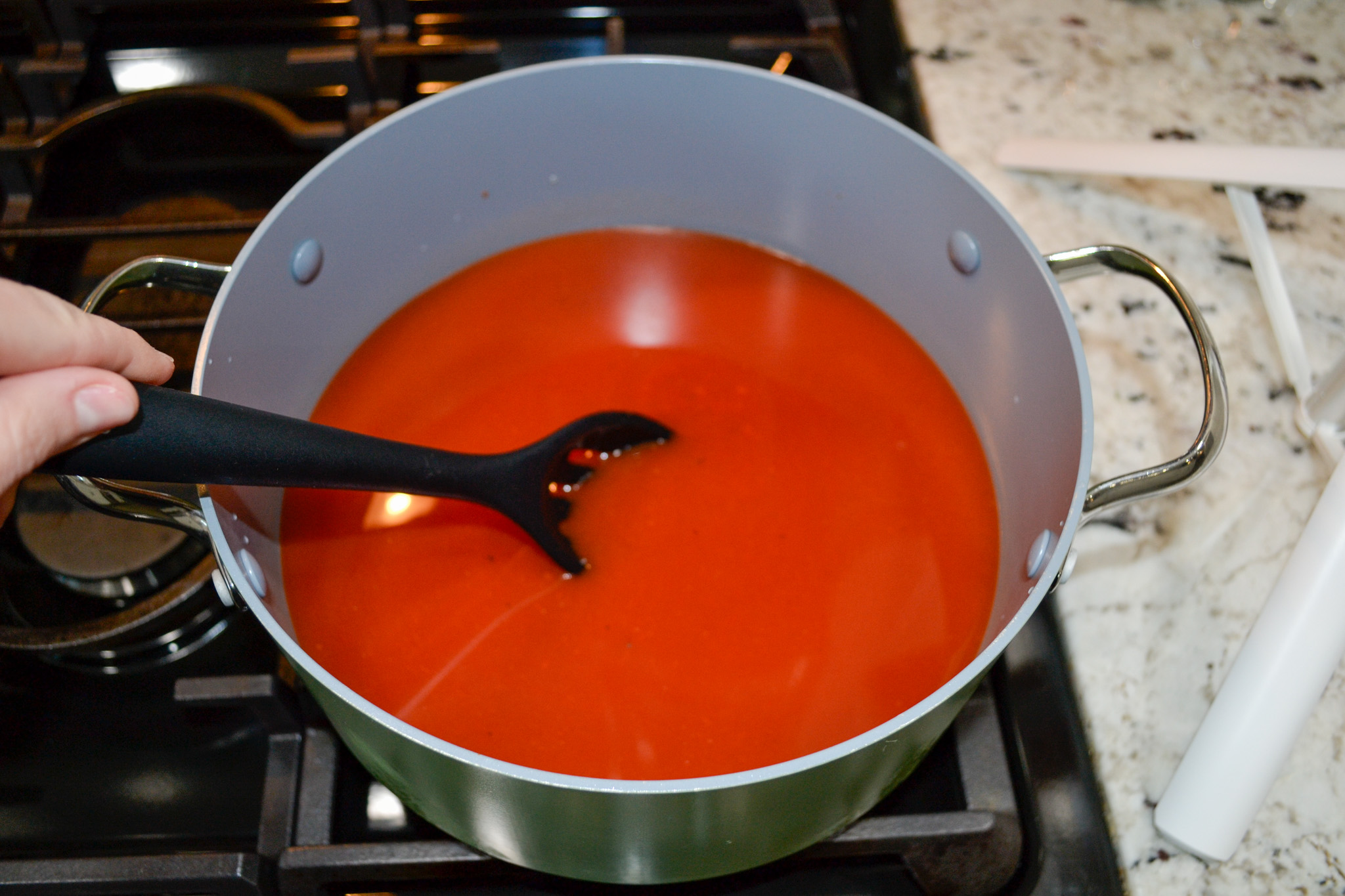 Stirring marinara sauce and chicken broth together in a large pot