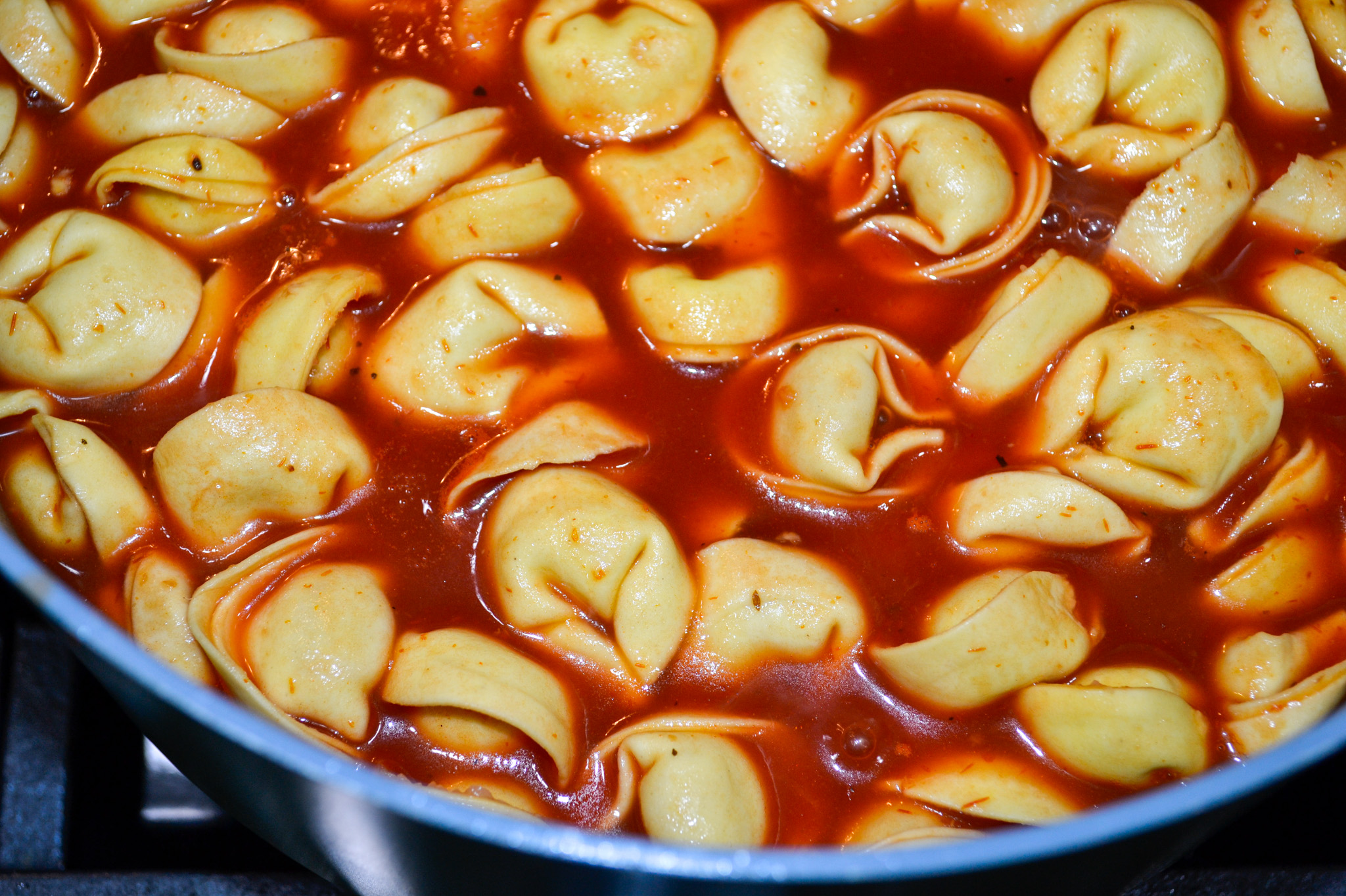 Cheese tortellini simmering in tomato broth on the stove