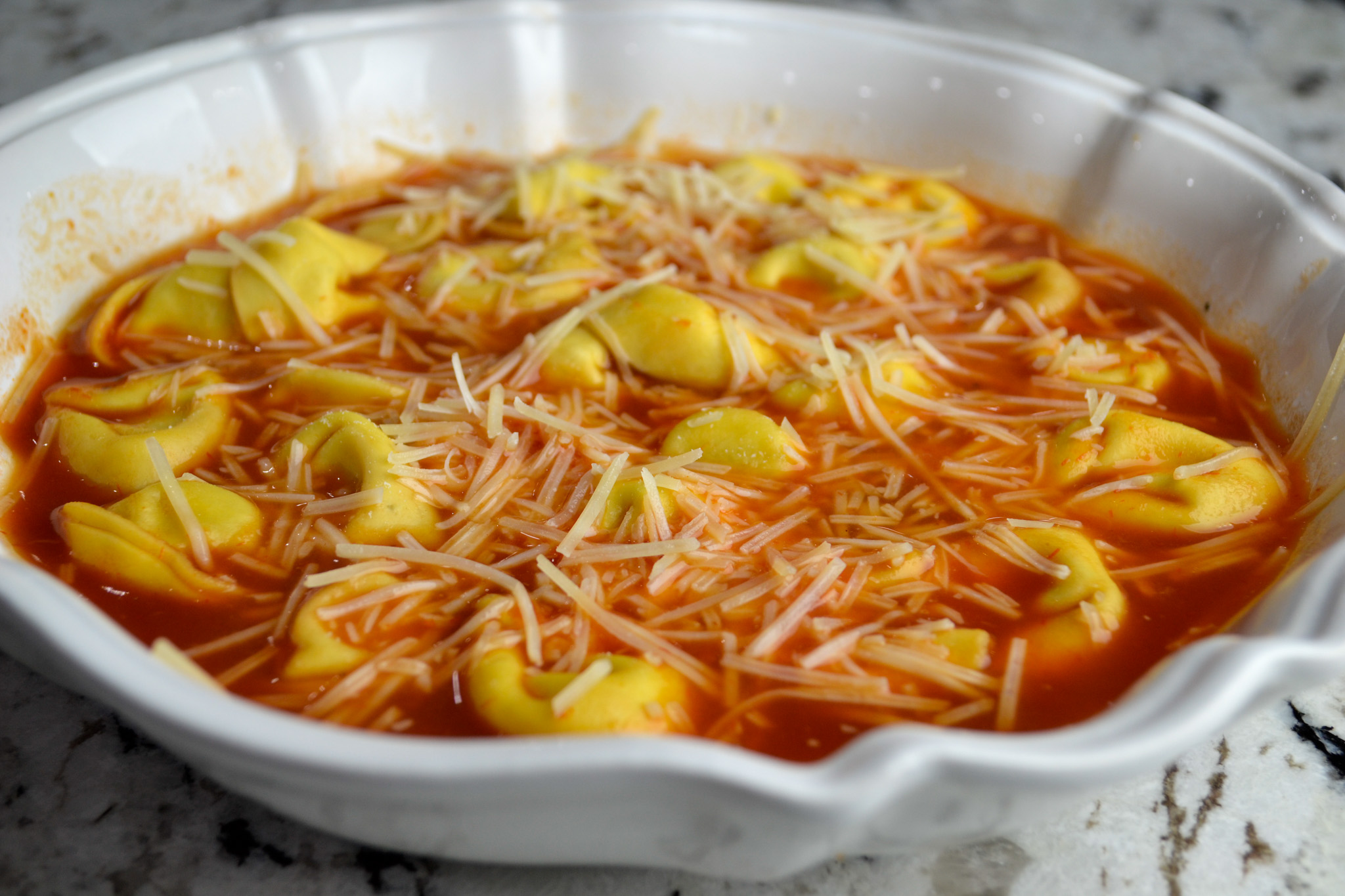 Cheese tortellini soup with tomato broth and Parmesan in a white serving dish