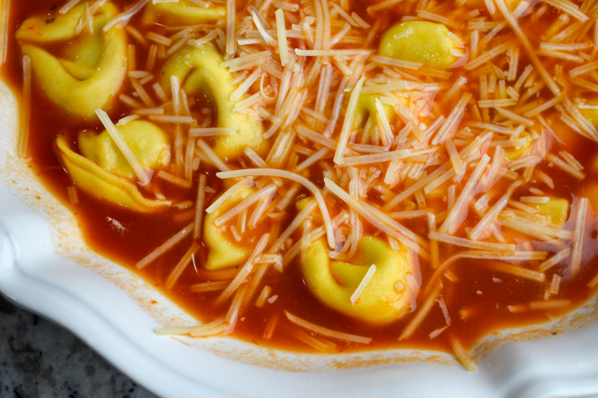 Close-up of cheese tortellini soup in creamy tomato broth topped with shredded Parmesan