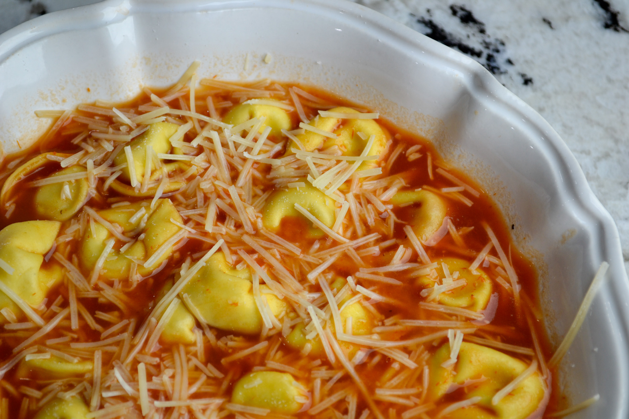 Bowl of cheese tortellini soup topped with Parmesan cheese