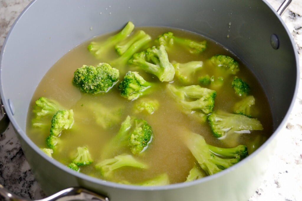 Frozen broccoli and chicken broth in a pot before simmering