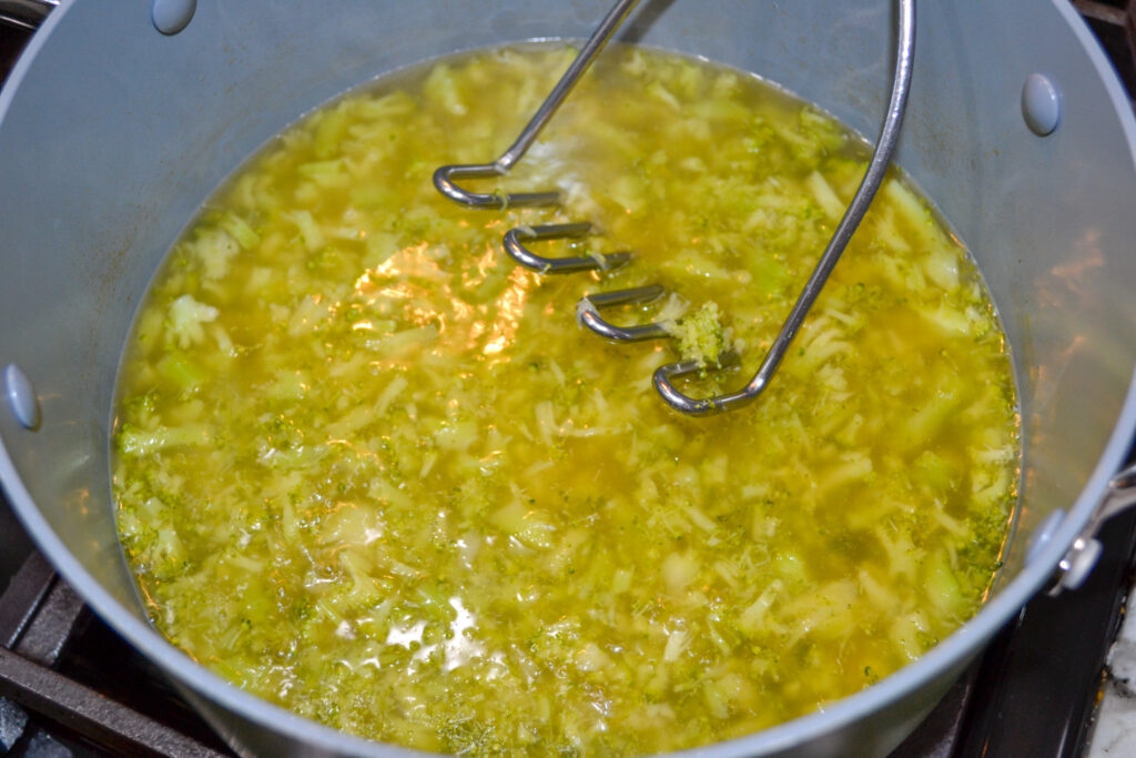 Mashing the cooked broccoli in the broth with a potato masher