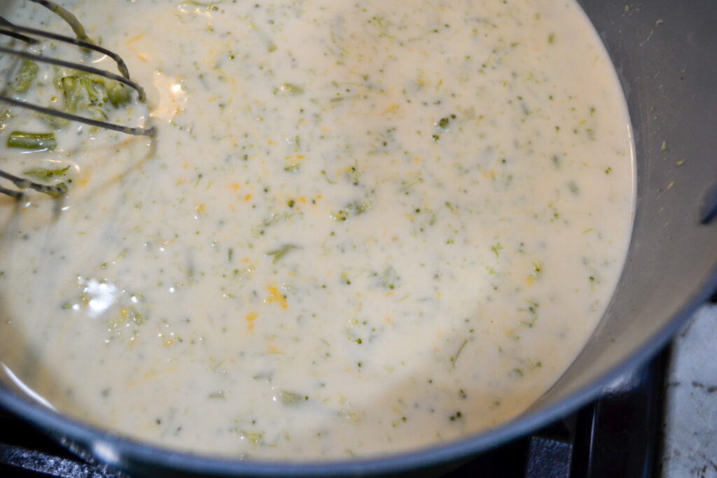 Creamy broccoli cheddar soup being whisked in the pot after the cheese melts