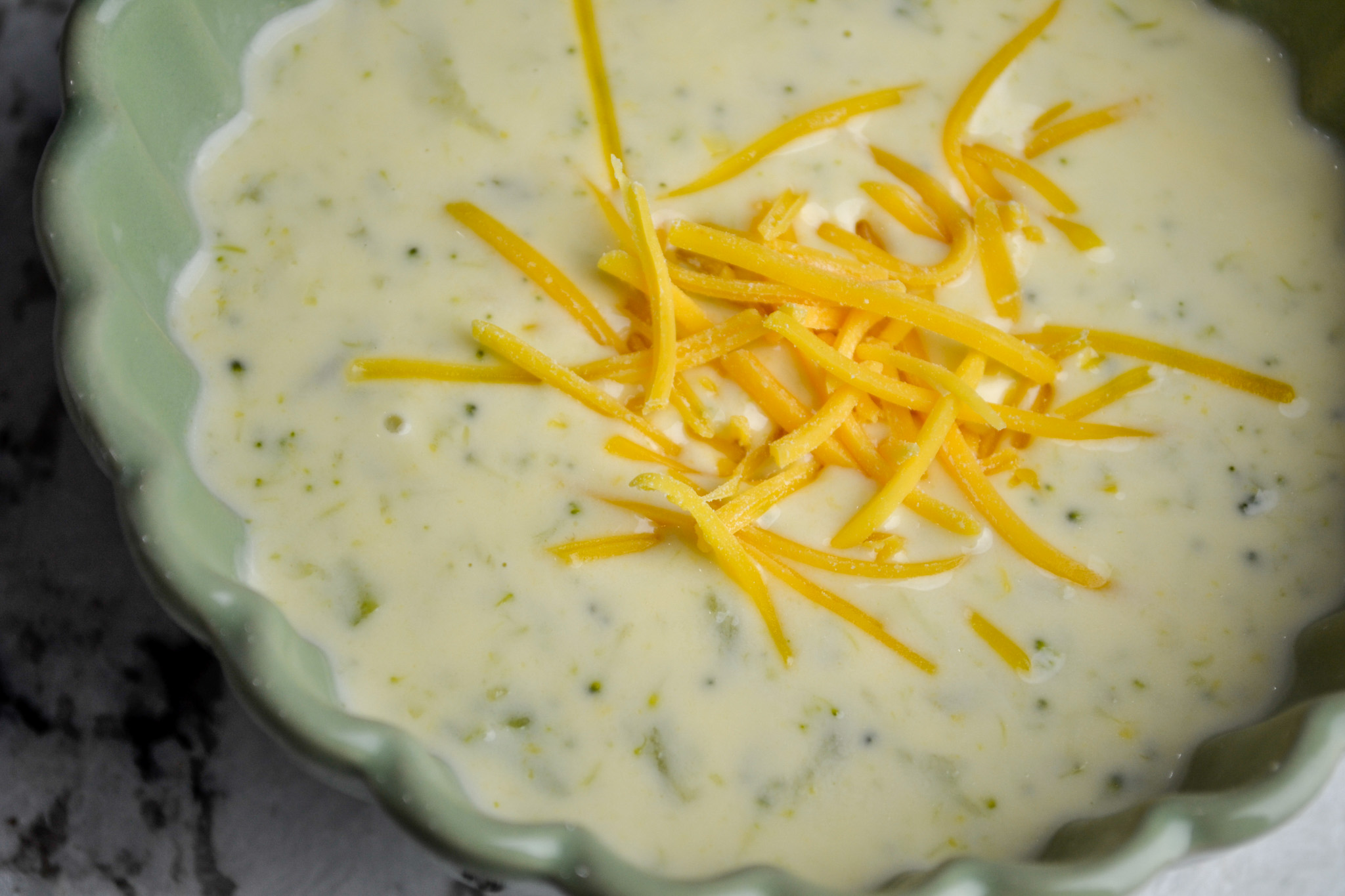 Close-up of creamy broccoli cheddar soup topped with shredded cheddar cheese