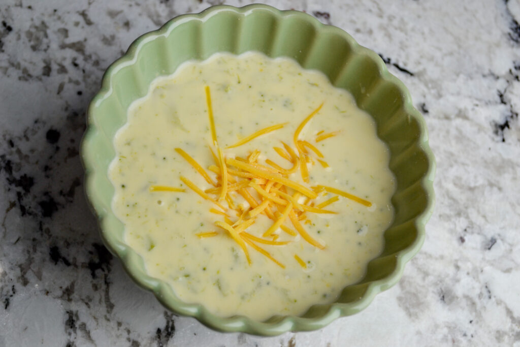 Broccoli cheddar soup in a green bowl on a marble counter