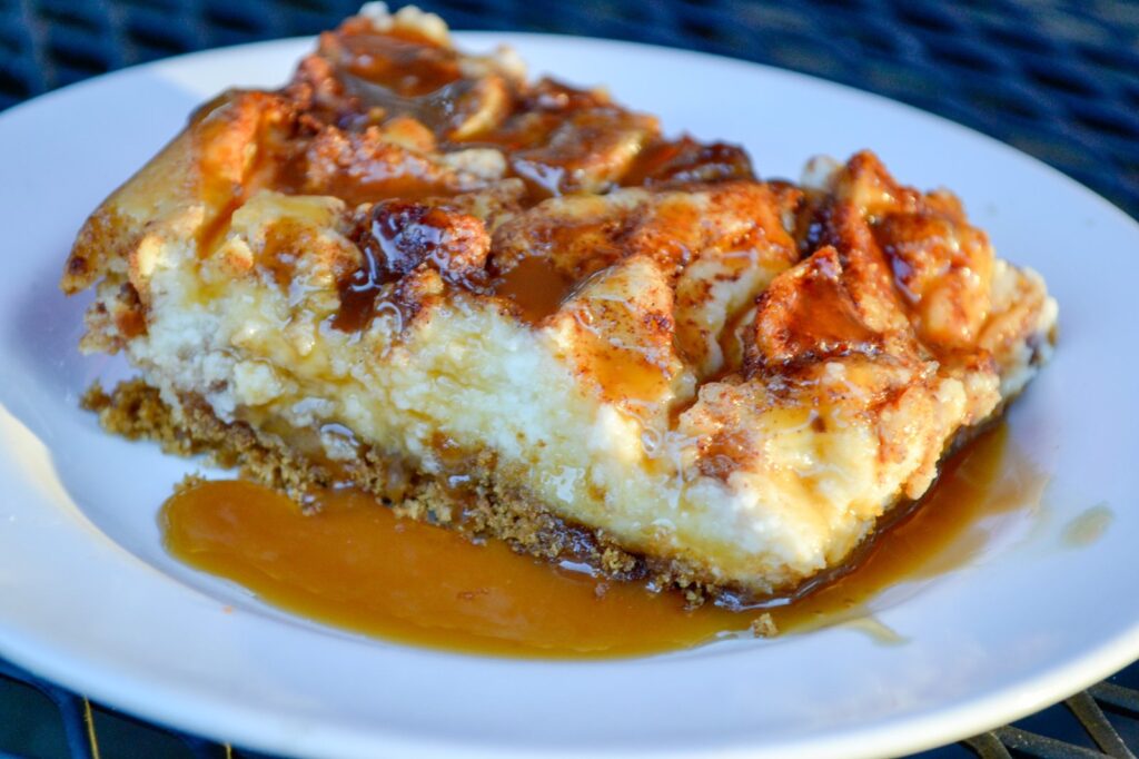 Close-up of a caramel apple cheesecake bar with caramel sauce pooling on a white plate
