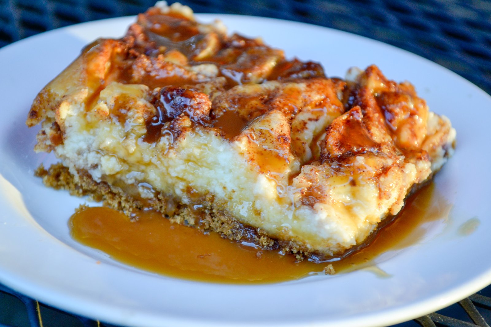 Close-up of a caramel apple cheesecake bar with caramel sauce pooling on a white plate