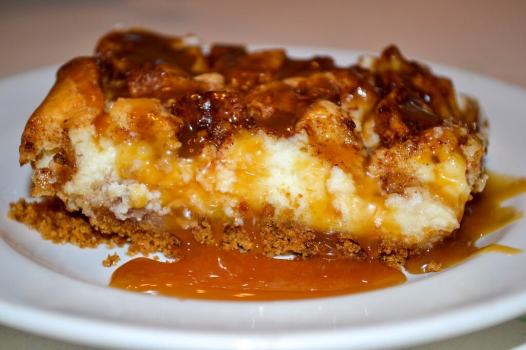 Caramel apple cheesecake bar showing the graham cracker crust, creamy cheesecake layer and caramel drizzle