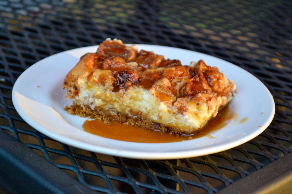 Caramel apple cheesecake bar with cinnamon apples and caramel sauce on a white plate outdoors