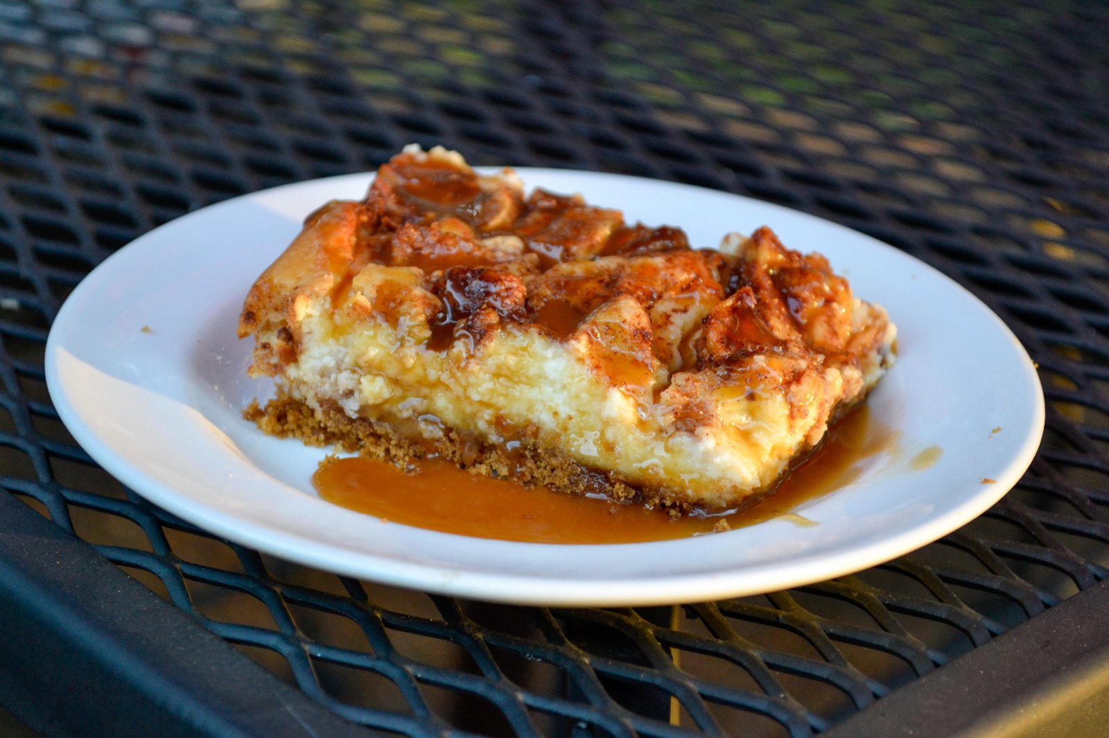Caramel apple cheesecake bar with cinnamon apples and caramel sauce on a white plate outdoors
