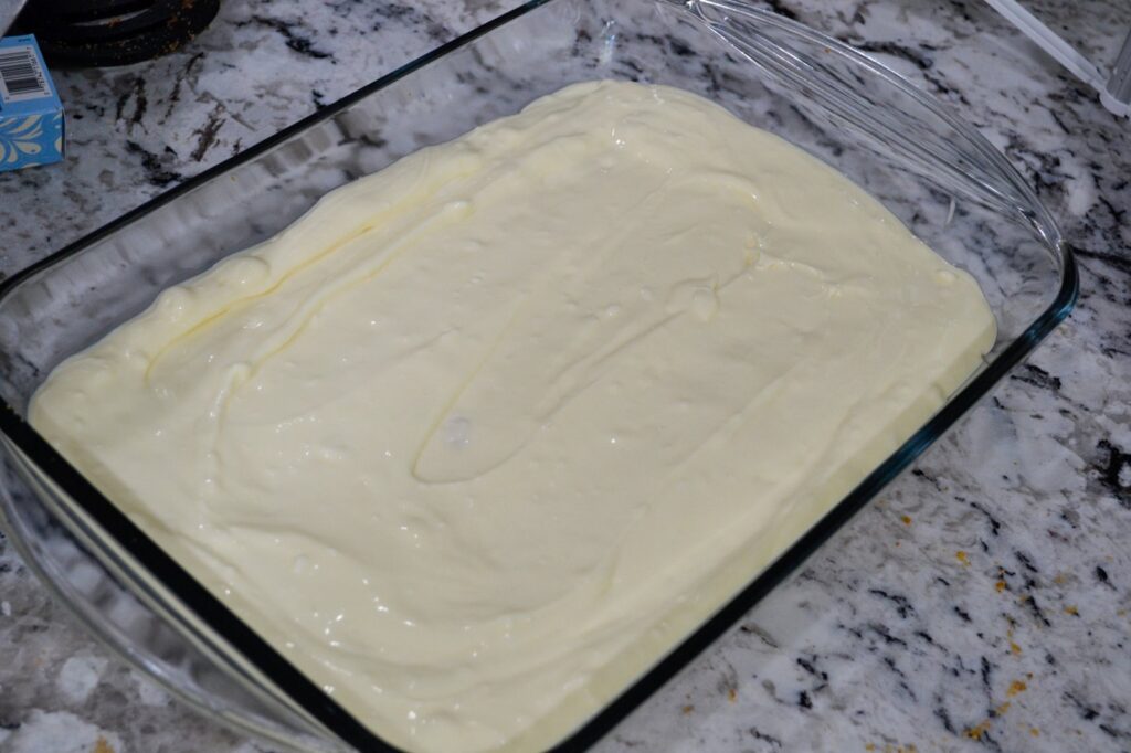 Cheesecake filling spread over a graham cracker crust in a glass 9x13 baking dish