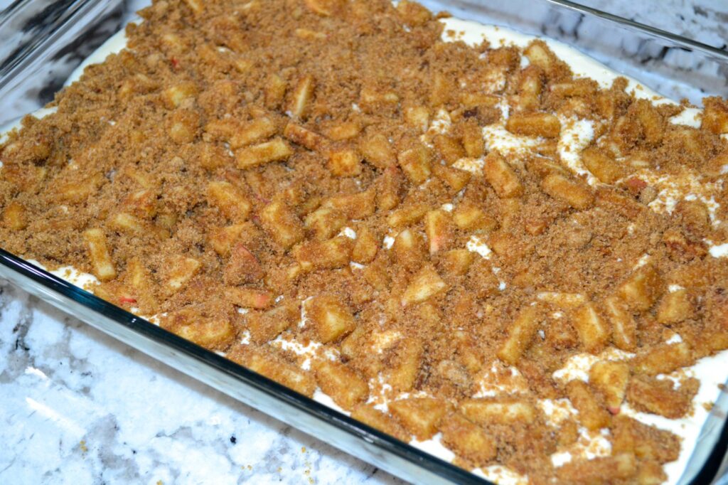 Cinnamon brown sugar apples scattered over cheesecake filling in a 9x13 pan before baking